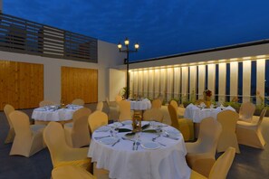 Een terras met ronde tafels, stoelen en een decoratieve muur met verticale panelen.