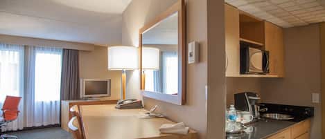 Une chambre d’hôtel équipée d’un bureau en bois, d’une télévision, d’un miroir, d’un four à micro-ondes et d’une kitchenette.