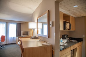Een hotelkamer met een houten bureau, een televisie, een spiegel, een magnetron en een kitchenette.