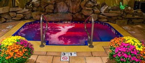 Een jacuzzi met metalen traptreden, omringd door kleurrijke bloemstukken en een stenen muur op de achtergrond.