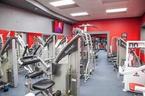 A gym with various exercise machines, a television screen, and red walls. - Ihotel & Conference Centre Red Deer (Red Deer)