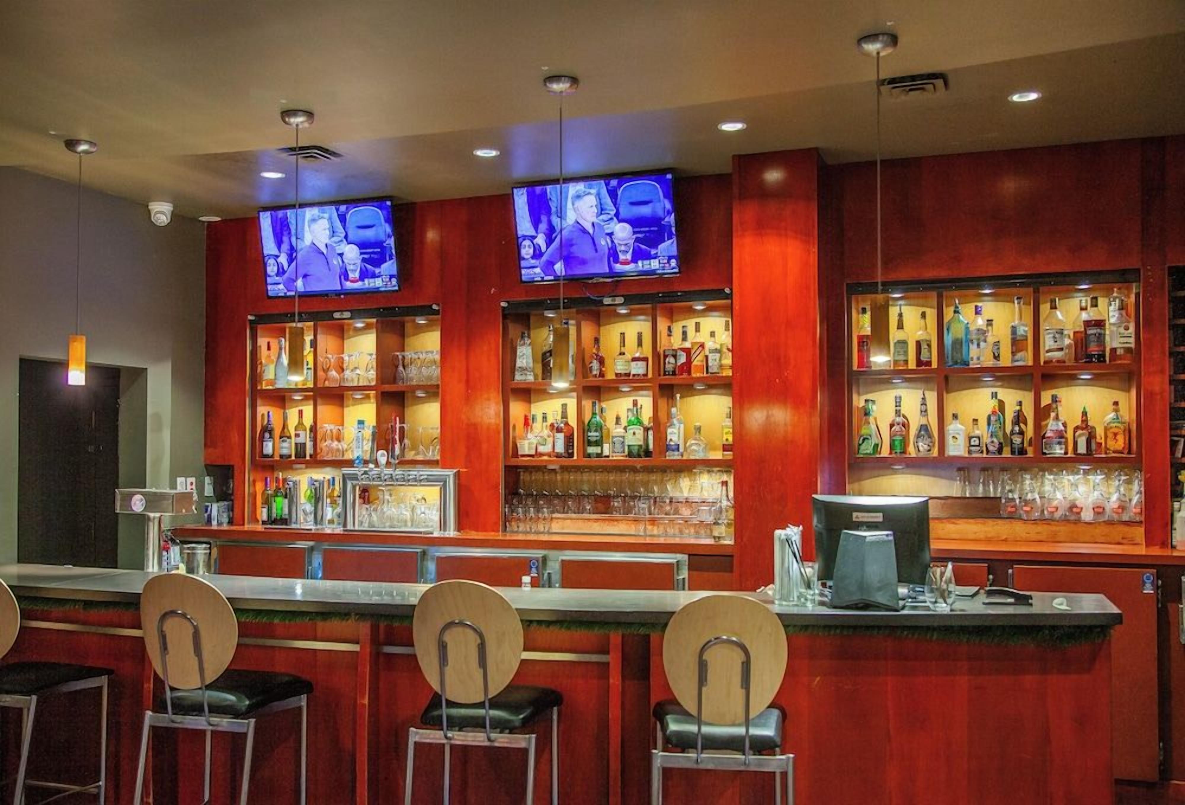 A bar area with multiple televisions, shelves of liquor, and bar stools.