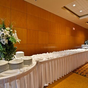 Een feesttafel met witte tafelkleden en borden, omringd door een houten muur en een vloerbedekking.
