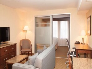 Een hotelkamer met een bank, een televisie, een bureau, een stoel en een schuifdeur naar een balkon.