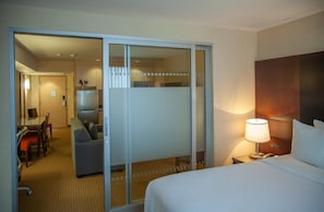Une chambre d’hôtel comprenant un lit, un bureau, une chaise, un canapé et une porte coulissante donnant accès à la salle de bain.
