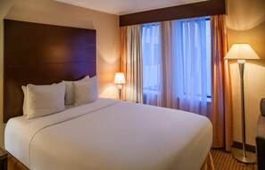 A hotel room with a large bed, a bedside table with a lamp, and a view of the outdoors through sheer curtains. - Ihotel & Conference Centre Red Deer (Red Deer)