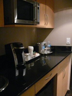 A kitchen with a microwave, coffee maker, and water bottles on the counter. - Radisson Red Deer Hotel (Red Deer)