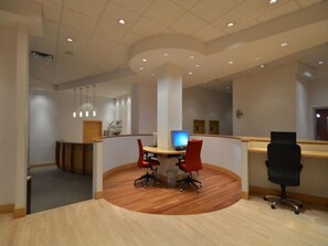 A modern conference room with a wooden floor, a round table, and red office chairs. - Ihotel & Conference Centre Red Deer (Red Deer)