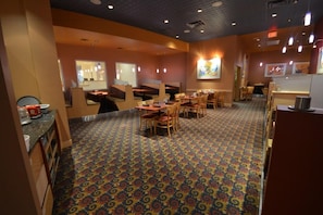 Un restaurant avec des banquettes et des tables, un tapis à motifs et un espace cuisine.