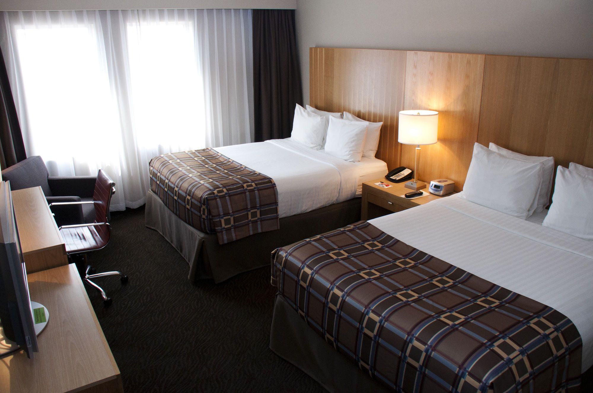 Ein Hotelzimmer mit zwei Betten, einem Schreibtisch, einem Stuhl, einer Lampe und einem Telefon.