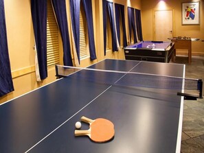 A ping pong table with a paddle and ball, a foosball table, and a door in a room with curtains. - Ihotel & Conference Centre Red Deer (Red Deer)