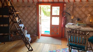 Ein gemütliches Interieur mit einer Holzleiter, einer zur Außenseite führenden Tür, einem kleinen Tisch mit Stuhl und einem an der Wand befestigten Feuerlöscher.