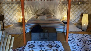 Eine Jurte mit Bett, Baldachin, Laternen und einem gemusterten Teppich.