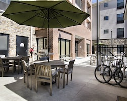 Un patio al aire libre con mesas y sillas, una parrilla, bicicletas y un edificio de piedra al fondo.
