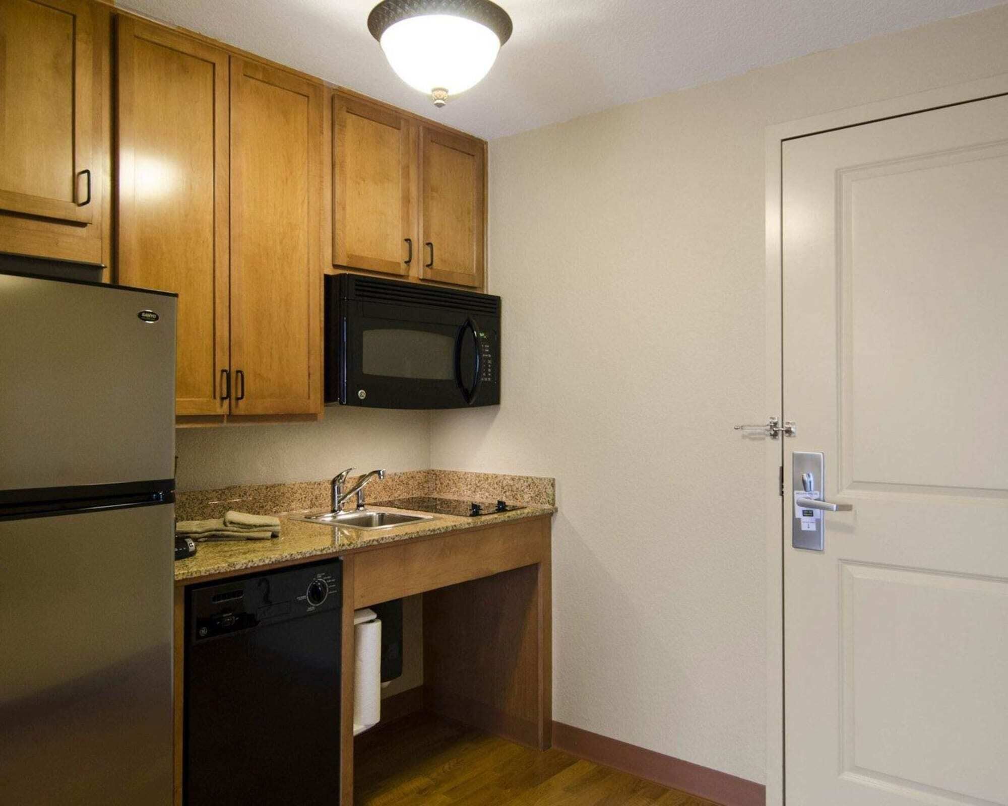 A compact kitchen with wooden cabinets, a built-in microwave, a stainless steel refrigerator, and a dishwasher.