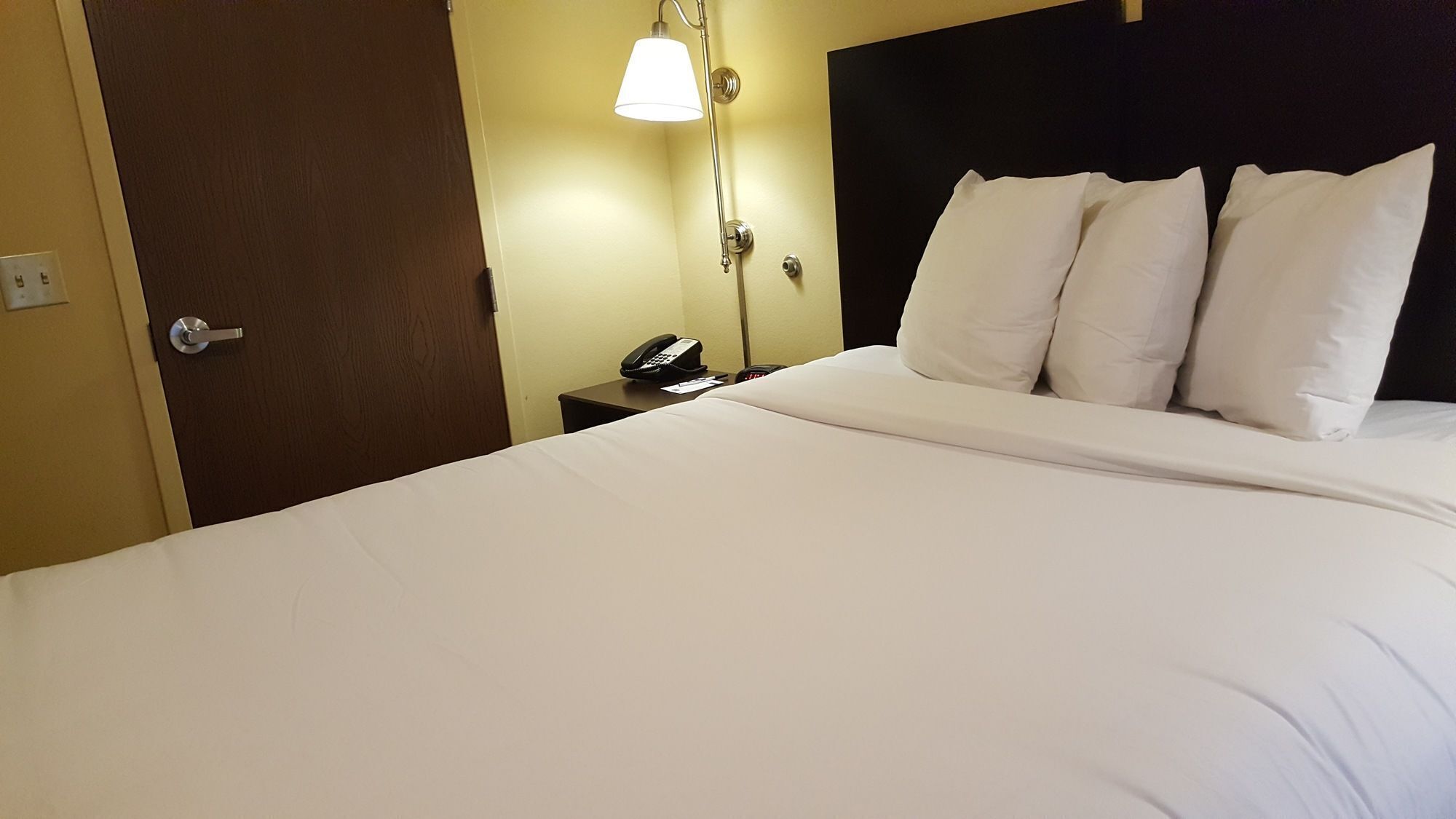 A hotel room with a bed, a bedside telephone, and a wall-mounted lamp.