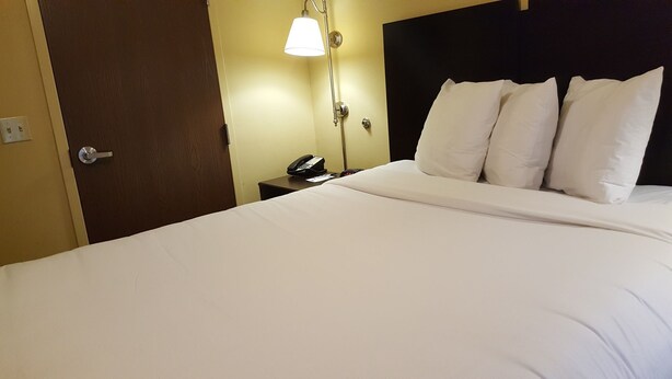 Ett hotellrum med en säng, en telefon vid sängen och en väggmonterad lampa.