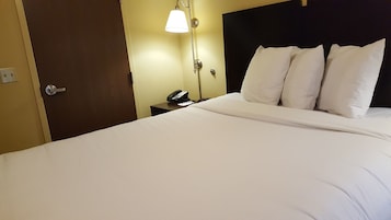 Una habitación de hotel con una cama, un teléfono en la mesita de noche y una lámpara de pared.
