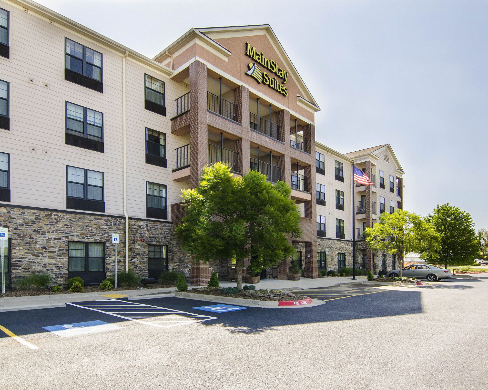 A multi-story hotel with a sign reading 'MarinStay Suites,' featuring a stone facade, multiple balconies, and a parking lot with handicapped parking spaces.