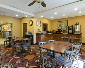 A hotel dining area with tables and chairs, a kitchen counter, and a clock on the wall. - Affordable Suites Rogers/bentonville, AR (Rogers)