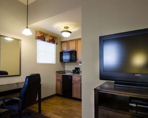 Habitación de hotel compacta con kitchenette, televisión de pantalla plana, zona de comedor con una silla y un espejo grande.