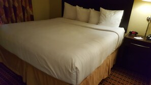 Una habitación de hotel con una cama grande, una mesita de noche con lámpara y un reloj.
