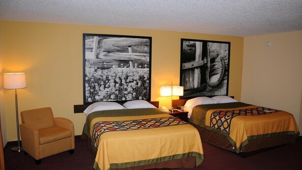 A hotel room with two beds, a chair, a nightstand with lamps, and two large black-and-white paintings on the walls.