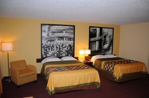 Habitación de hotel con dos camas, una silla, una mesita de noche con lámparas y dos grandes cuadros blanco y negro en las paredes.