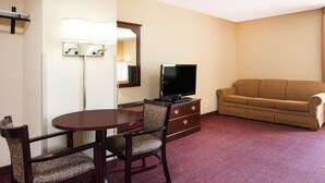 A hotel room with a round dining table, two chairs, a sofa, a TV on a dresser, and a mirror on the wall.