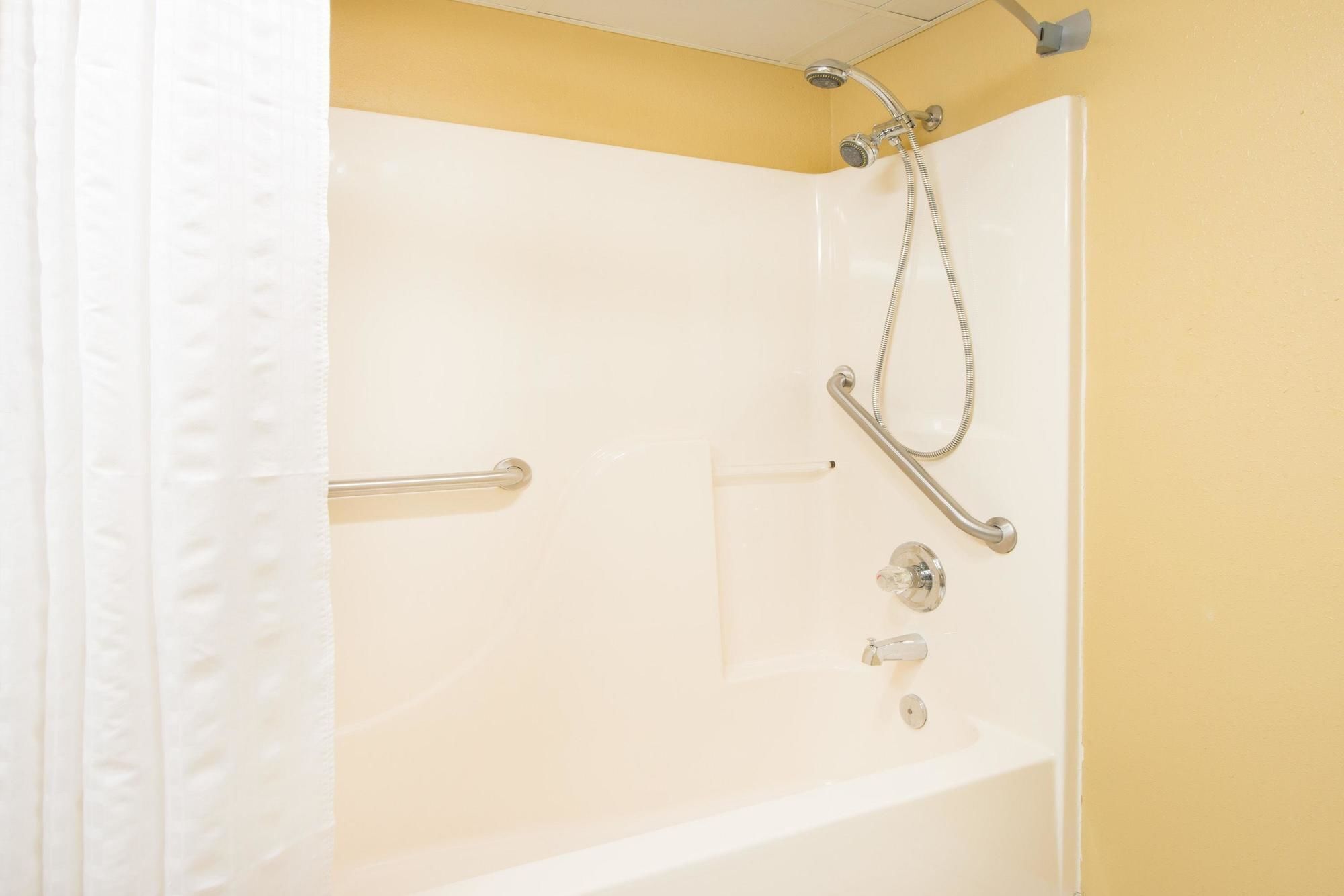 A white bathtub with a shower head and grab bars.