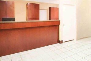 A reception area with a counter, wooden cabinets, and a tiled floor. - Super 8 by Wyndham Lamar (Lamar)