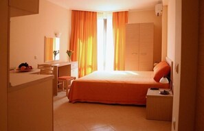 Hotellihuone, jossa on sänky, työpöytä, tuoli, vaatekaappi ja ikkuna, jossa on verhot.