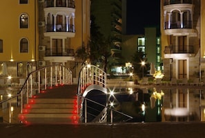 Vista nocturna de un hotel con piscina, una escalera con luces rojas y balcones.
