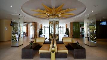 A lobby with a central seating area, a unique ceiling design, and a large mirror reflecting the space.