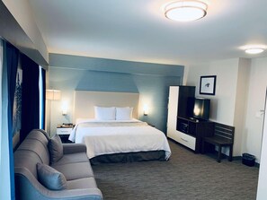 Ein Hotelzimmer mit Bett, Sofa, Schreibtisch, Fernseher und einem Bild an der Wand.
