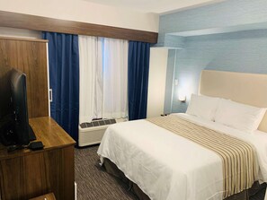 Ein Hotelzimmer mit einem Bett, einem Fernseher auf einem Holztisch, einem Heizgerät und einem Fenster mit Vorhängen.