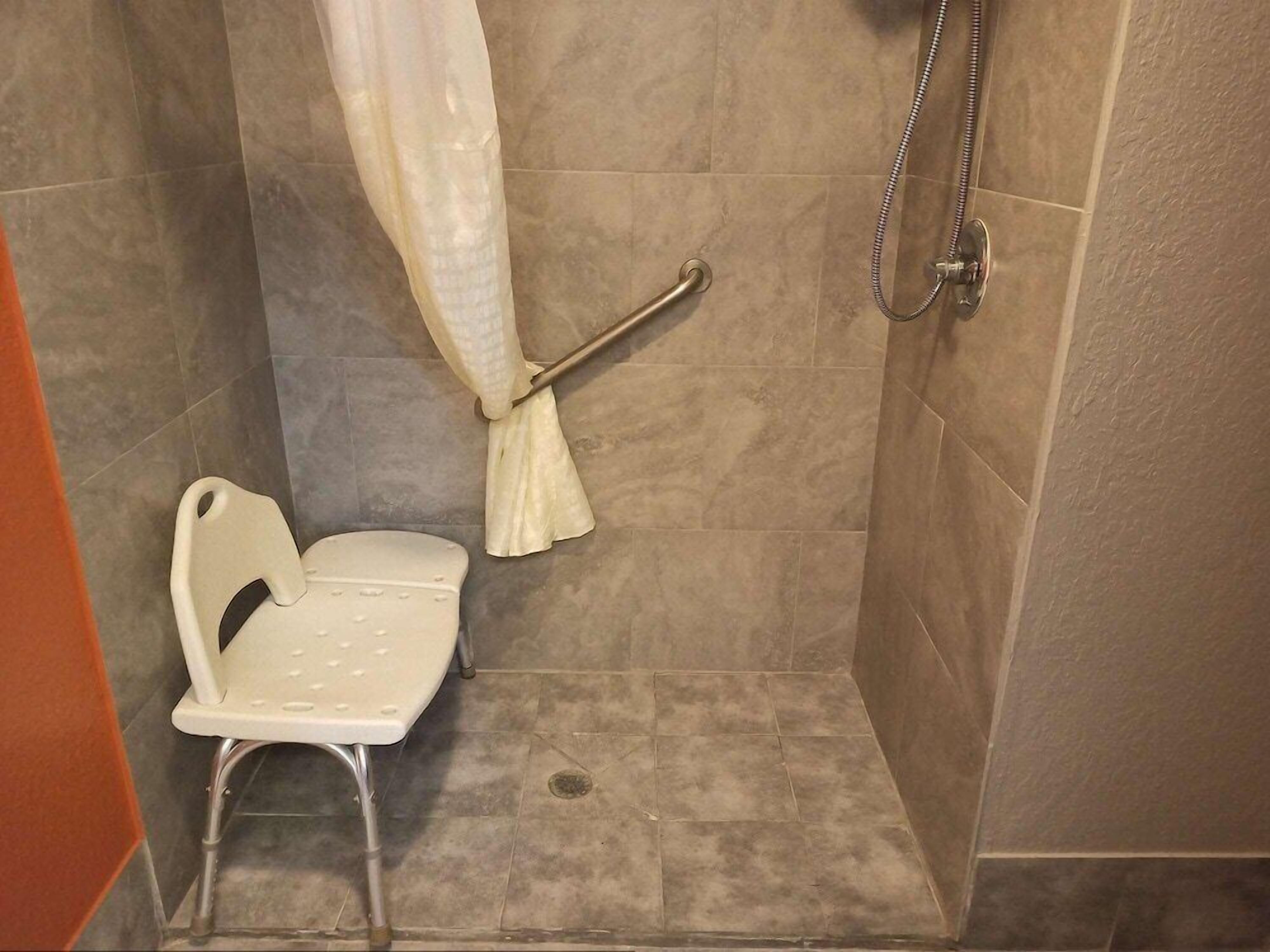 A shower stall with a grab bar, a white chair, and a shower curtain.