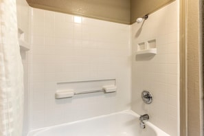 Une salle de bain avec des murs recouverts de carreaux blancs, une baignoire, un porte-serviettes et un rideau de douche.