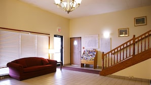 A hotel lobby with a red sofa, a wooden staircase, a map on the wall, and an exit sign.