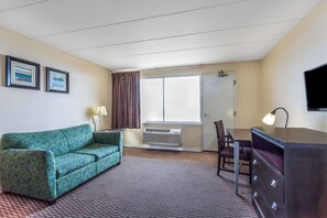 Hotelkamer met een bank, bureau, stoel, lamp, televisie en een raam met gordijnen.