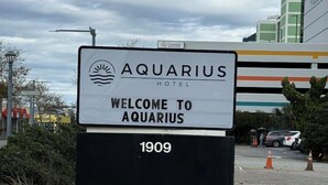 A sign for the Aquarius Hotel with a sun and water wave logo, welcoming visitors. - Travelodge by Wyndham Suites Virginia Beach Oceanfront (Virginia Beach)