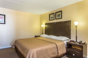 Een hotelkamer met een groot bed, twee bedlampjes, een nachtkastje met een telefoon en een klein tafeltje, en twee ingelijste foto's aan de muur.