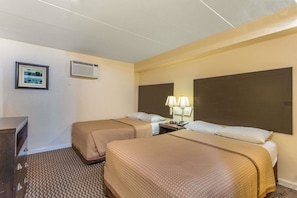 A hotel room with two beds, a desk, a framed picture, an air conditioning unit, and a nightstand with lamps. - Travelodge by Wyndham Suites Virginia Beach Oceanfront (Virginia Beach)