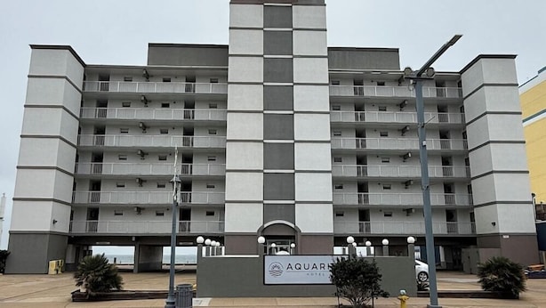 A multi-story hotel with a central tower, balconies, and a sign for the Aquamar Hotel. - Travelodge by Wyndham Suites Virginia Beach Oceanfront (Virginia Beach)