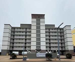 Um hotel de vários andares com uma torre central, varandas e uma placa com o nome Aquamar Hotel.