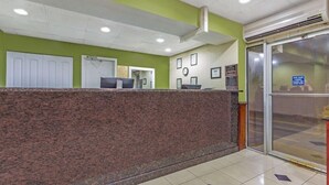 A reception area with a marble counter, a clock, framed pictures, and a glass door. - Travelodge by Wyndham Suites Virginia Beach Oceanfront (Virginia Beach)