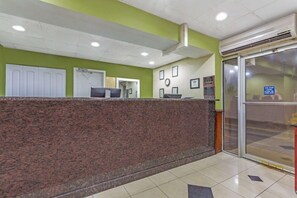 Un área de recepción con mostrador de mármol, un reloj, cuadros enmarcados y una puerta de cristal.