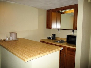 A small kitchen with wooden cabinets, a sink, a microwave, and a coffee maker. - Motel6 Oriskany, NY (Oriskany)