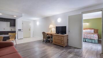 A compact living space with a kitchenette, a desk with a lamp, a television, a sofa, and a bed.