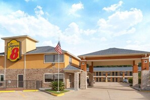 A Super 8 hotel with a flag, a parking lot, and a building entrance.
